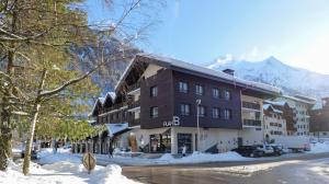 a large building in the snow with mountains in the background at Plan B Hotel - Living Chamonix in Chamonix-Mont-Blanc