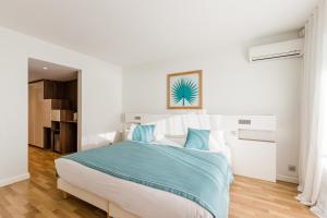 a white bedroom with a large bed with blue pillows at Hôtel Hélios in Juan-les-Pins