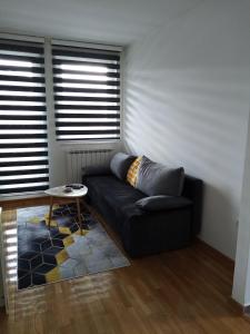 a living room with a black couch and two windows at Apartman Dunjica in Pale