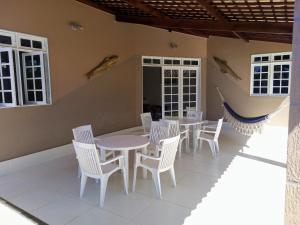 eine Terrasse mit weißen Stühlen, Tischen und einer Wand in der Unterkunft Casa das Conchas Ipioca in Maceió