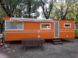 un rimorchio arancione con panchina e tavolo di Camping Sabanell a Blanes