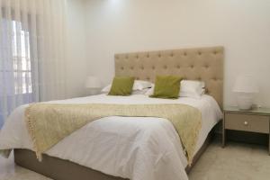 a white bedroom with a large bed with green pillows at Amazing one Bedroom Apartment in Amman Elwebdah 5 in Amman