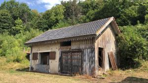 ein altes Holzgebäude mit einer Tür auf einem Feld in der Unterkunft L'ECURIE du Château in Lebétain