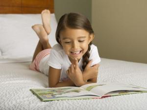 una niñita acostada en una cama leyendo un libro en WoodSpring Suites College Station, en College Station