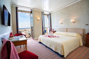 Cette chambre comprend un lit, un bureau et une fenêtre. dans l'établissement Hotel Splendid, à Cannes