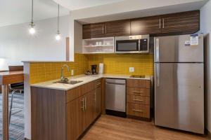 MainStay Suites Carlsbad South في كارلسباد: مطبخ مع دواليب خشبية وثلاجة حديد قابلة للصدأ
