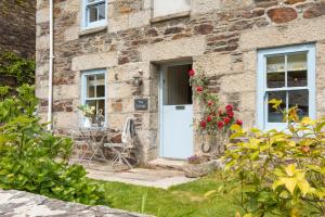 a stone cottage with a white door and flowers at Navas Nook in Falmouth