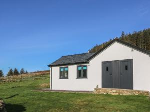 a white barn with a grey door and a grass field at The Sail Loft in Pwllheli