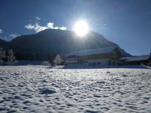 a building in the snow with the sun behind it at Riederhof in Ruhpolding