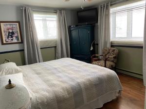 a bedroom with a bed and a chair and windows at Gite Chute Couette Cafe in Notre-Dame-du-Portage