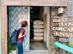 a woman with a backpack standing outside of a store at Guest House Cam Cam Okinawa in Naha