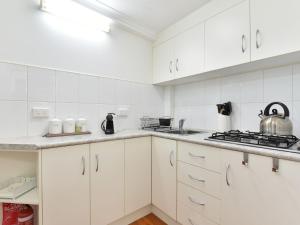 a white kitchen with white cabinets and a stove at Olive Grove 1 Studio in Pokolbin