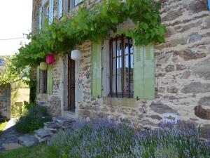 a stone house with green windows and purple flowers at Holiday home in the forest in Auzat