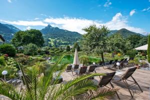 a patio with chairs and an umbrella and mountains at Hotel Vitalquelle Montafon in Schruns-Tschagguns
