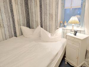 een slaapkamer met een bed met witte kussens en een raam bij Ferienwohnung *Fenja* in Norddorf