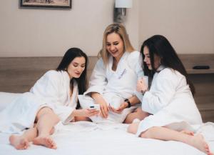 três mulheres em roupões brancos sentadas numa cama em Summit Apart Hotel em Kiev