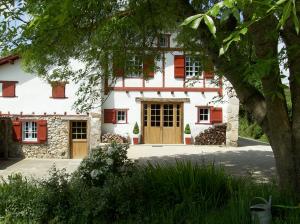una casa blanca con persianas rojas y un árbol en Maison Anderetea, en Mendionde