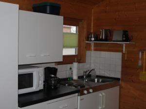 eine Küche mit weißen Schränken, einer Spüle und einer Mikrowelle in der Unterkunft Pretty Bungalow in Neubukow with Garden, Roof Terrace, BBQ in Neubukow