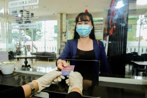 a woman wearing a face mask holding a credit card at Serela Cihampelas by KAGUM Hotels in Bandung