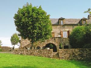 an old stone house with a stone wall and a tree at Cosy holiday home with garden in Saint-Geniez-dʼOlt