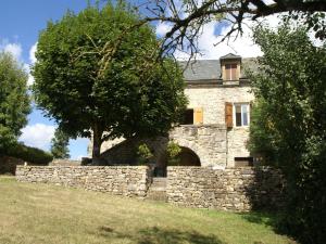 a stone house with a stone wall and a tree at Cosy holiday home with garden in Saint-Geniez-dʼOlt