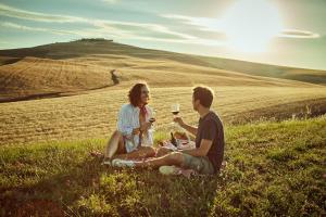 un hombre y una mujer sentados en un campo con copas de vino en Agriturismo Lunadoro, en Monticchiello