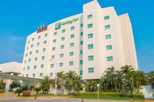Holiday Inn Acapulco La Isla, an IHG Hotel في أكابولكو: مبنى ابيض كبير امامه نخيل