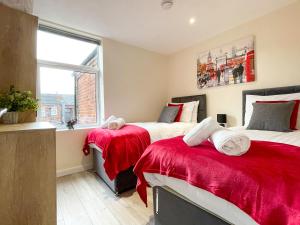 a bedroom with two beds with red sheets and a window at Spacious 4-bed house in Crewe by 53 Degrees Property, ideal for Contractors & Business, FREE parking - sleeps 7 in Crewe