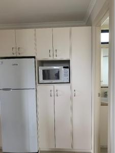 a white kitchen with a microwave and a refrigerator at Beach Cabin Apollo Bay in Apollo Bay