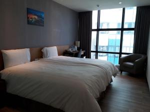 um quarto com uma grande cama branca e uma cadeira em Honest & Warm Hotel em Taoyuan