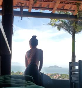 a woman looking out of a window at the ocean at Bella Vista Eco Experience in Búzios