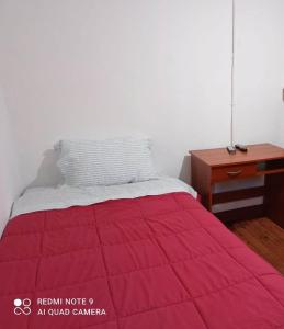 a bed with a red blanket and a desk at Hospedaje curicó casa grande in Curicó