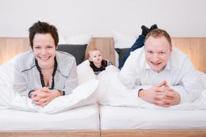 two people sitting on a bed with a baby at Am Landhof Heiligenstadt Ferienwohnung in Heilbad Heiligenstadt