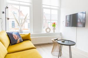 sala de estar con sofá amarillo y TV en By de Buurvrouw, en Kollum