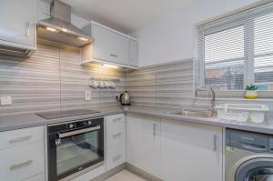 a kitchen with white cabinets and a sink and a dishwasher at Kentmere Apartment Thamesmead in Thamesmead