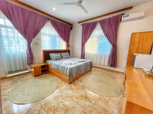 a bedroom with a bed with purple curtains and two windows at Max Hotel Nungwi in Nungwi