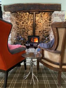two glasses of wine on a table in front of a stone fireplace at Combe House Hotel in Holford