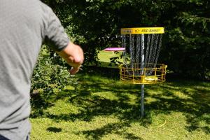 a person throwing a frisbee into a frisbee golf basket at Lydde Gård in Kinna