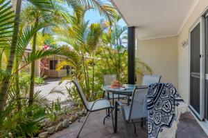 a patio with a table and chairs and palm trees at Lychee Tree Holiday Apartments in Port Douglas