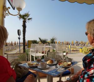two people sitting at a table with food on the beach at Hotel Strand a frontemare in Lido di Jesolo