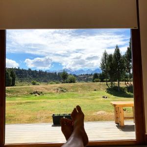 una persona sentada en el alféizar de una ventana mirando hacia un campo en Wau Purul, Cabaña 2 en Cholila