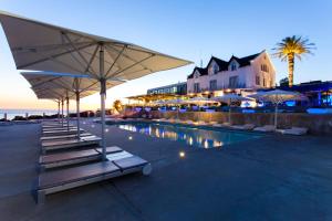 a pool with chairs and umbrellas and a building at Farol Hotel in Cascais