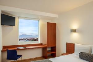 a room with a bed and a desk and a window at One Puebla FINSA in Puebla