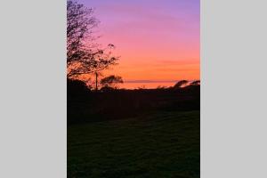 una puesta de sol sobre un campo con un árbol en primer plano en Lle Mary - Beautiful views, Hot tub, Secluded, Dog Welcome, Barmouth, en Llanddwywe