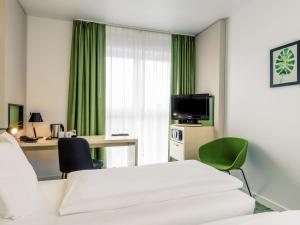 a room with a bed, chair, desk and television at Mercure Hotel Hannover Mitte in Hannover