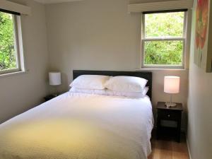 a bedroom with a white bed with two windows at Lake Rotoehu Accommodation - Lake Rotoehu Home in Rotoiti