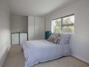 a bedroom with a bed with striped sheets and a window at Waikanae Retreat - Waikanae Beach Holiday Home in Waikanae