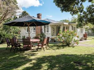 a table and chairs with an umbrella in front of a house at Onetangi Beach Cottage - Onetangi Bach in Onetangi