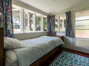 a bedroom with windows and a bed and a rug at Onetangi Beach Cottage - Onetangi Bach in Onetangi