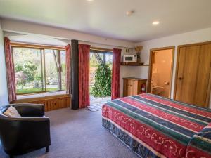 a bedroom with a bed and a chair and windows at Tasman Hideaway - Marahau Holiday Home in Marahau